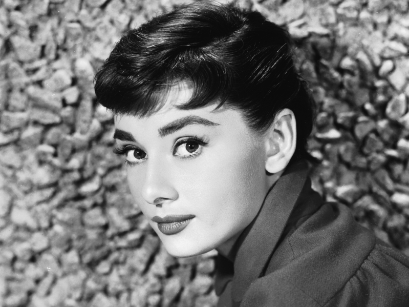 Audrey Hepburn sitting in front of brick wall