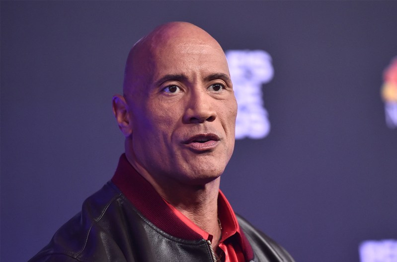 Dwayne "The Rock" Johnson in a red shirt and leather jacket, looking stunned.