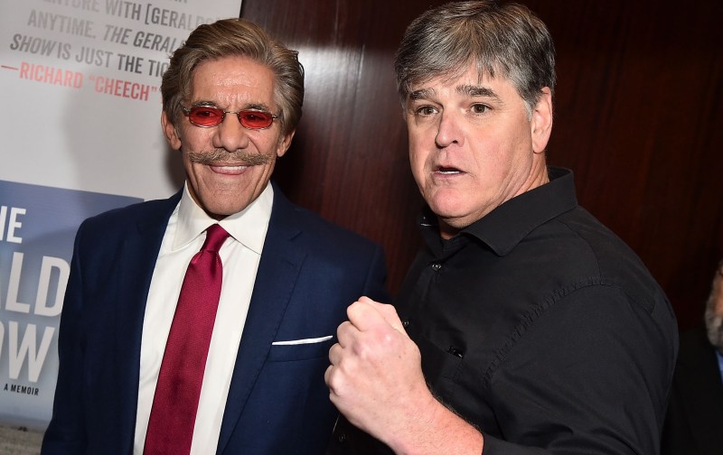 Geraldo Rivera wears a navy suit and red tie as he stands with Sean Hannity, in a black shirt
