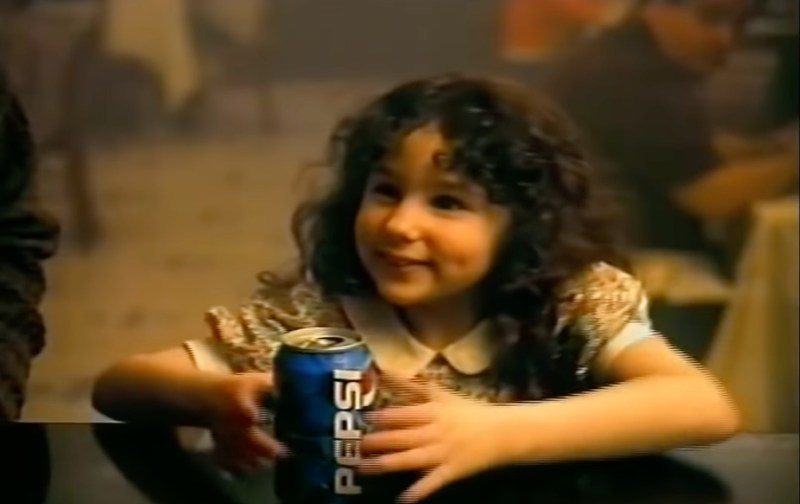 Hallie Eisenberg wears a floral dress and grabs a can of Pepsi in a commercial