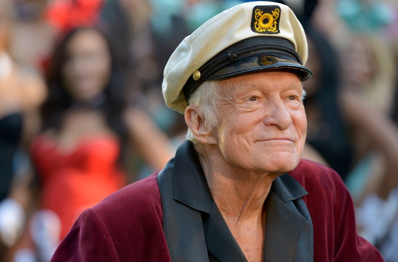 Hugh Hefner smiling, in a red robe and captain's hat