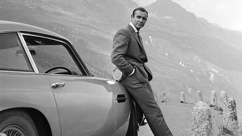 Sean Connery posing on set as James Bond, leaning on the famous Aston Martin