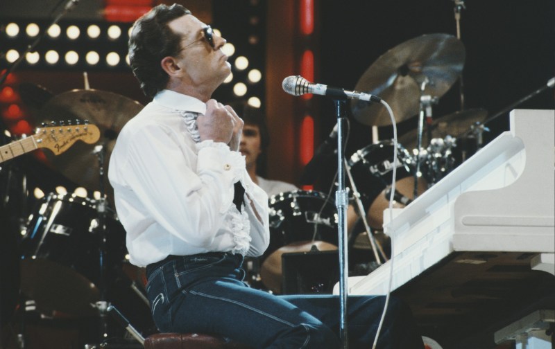 Jerry Lee Lewis adjusts his collar as he sits in front of a white piano