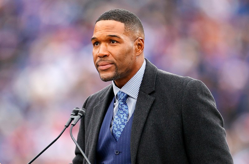 Michael Strahan looking serious while making a speech in a suit.