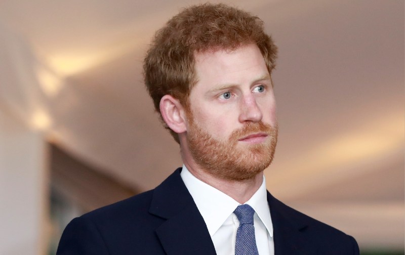 Prince Harry wears a dark suit and blue tie during an indoor event