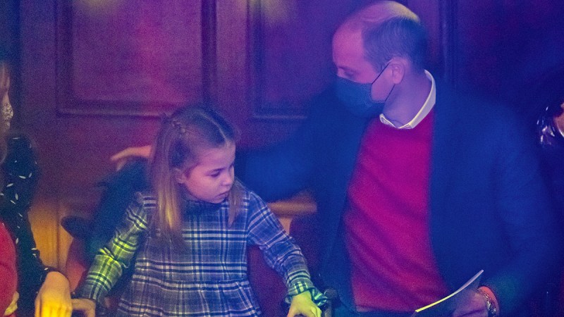 Prince William on the right in a mask, sitting at a play with Princess Charlotte
