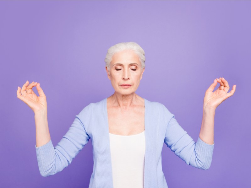 Beautiful nice gray-haired old peaceful lady wearing casual, closed eyes, meditating, praying. Isolated over pastel violet purple background