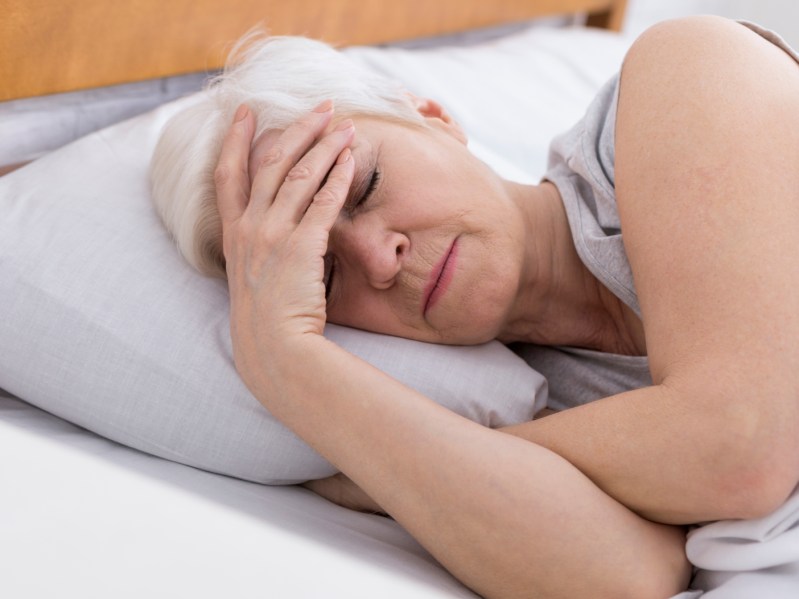 Worried senior woman suffering from insomnia, having headache in bed, touching her forehead