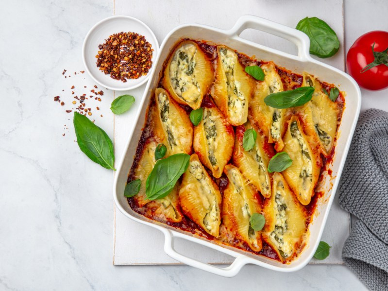 Ricotta and spinach stuffed shell pasta with tomato sauce in white baking dish, white background, top view
