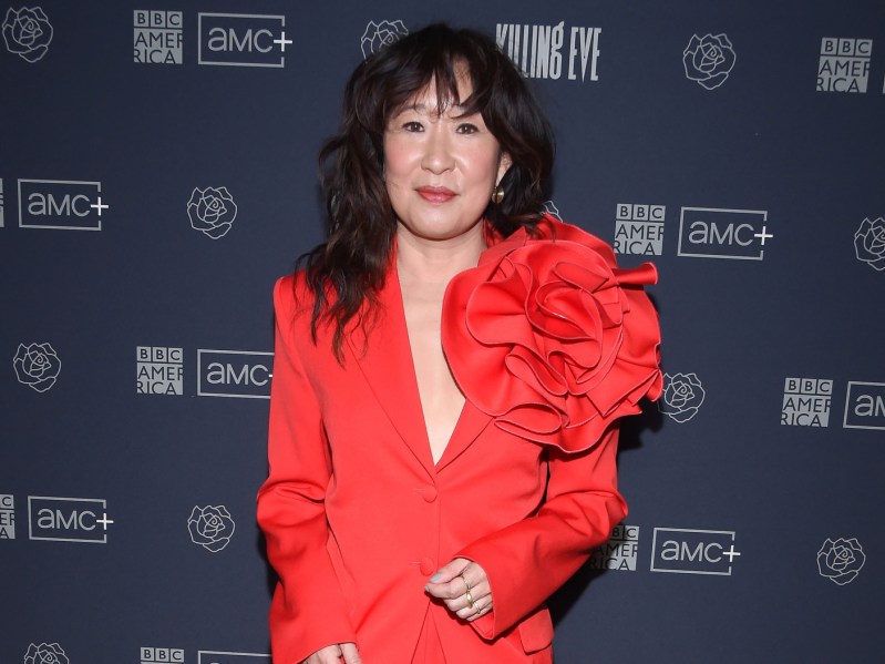 Sandra Oh standing on the red carpet wearing a red jumpsuit