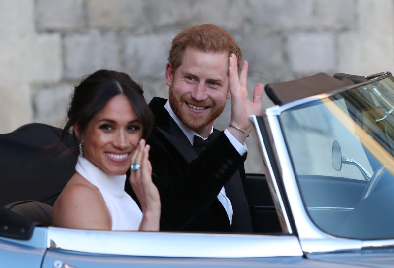 WINDSOR, UNITED KINGDOM - MAY 19: Duchess of Sussex and Prince Harry, Duke of Sussex wave as they leave Windsor Castle after their wedding to attend an evening reception at Frogmore House, hosted by the Prince of Wales on May 19, 2018 in Windsor, England.