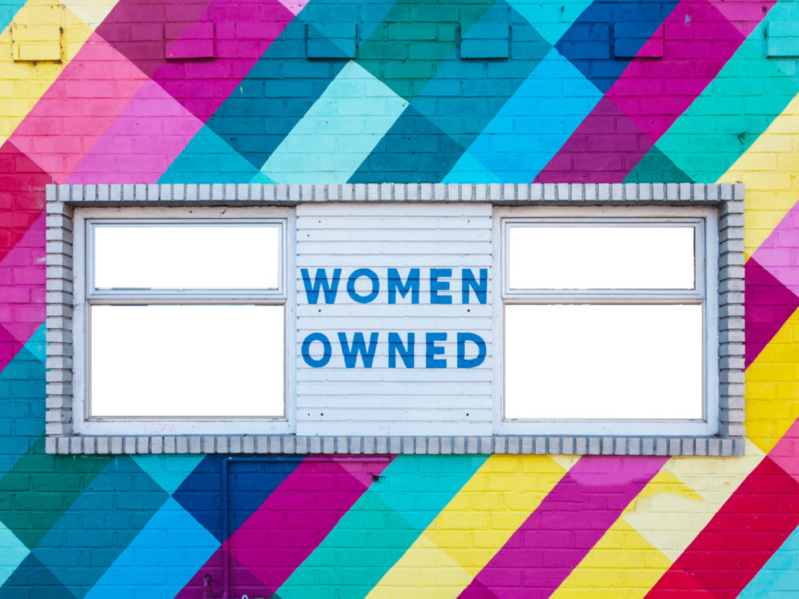 Colorful brick wall with "women owned sign" on it