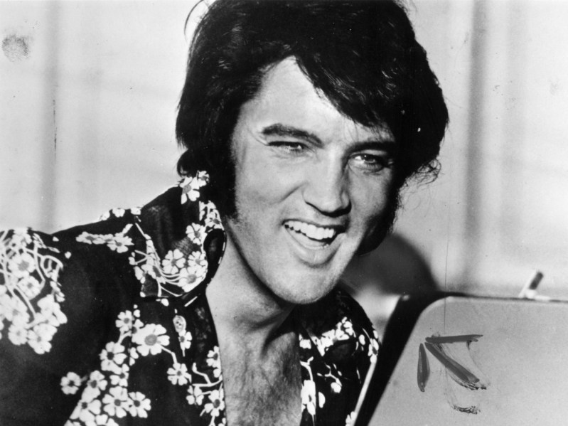 Black and white photo of Elvis Presley laughing, wearing floral print shirt
