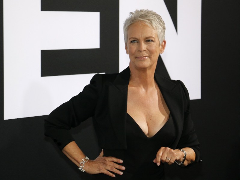 Jamie Lee Curtis wears a black dress and points downward on the red carpet