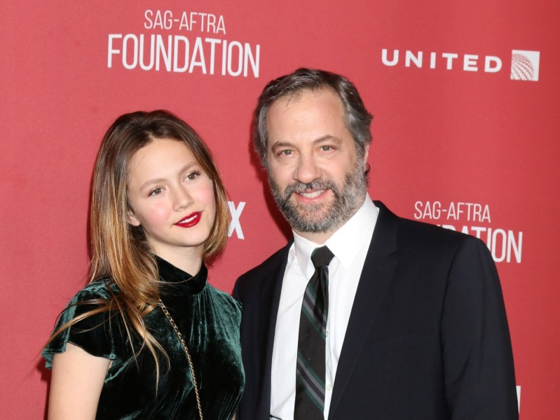Iris Apatow (L) and Judd Apatow (R) dressed formally against a red background