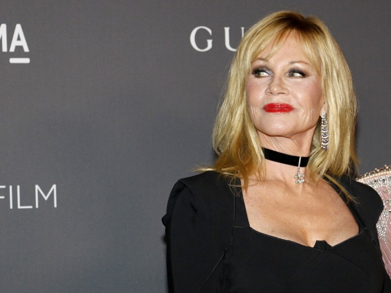 Melanie Griffith smiles in black dress and red lipstick