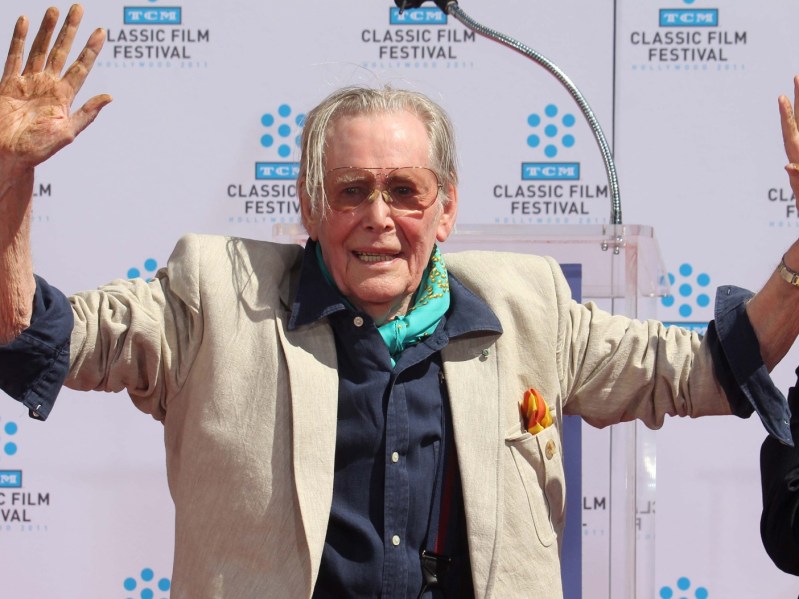 Peter O'Toole standing outside in sun glasses holding his hands up
