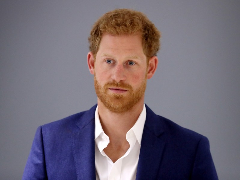 Prince Harry wears a blue suit and no tie against a gray background
