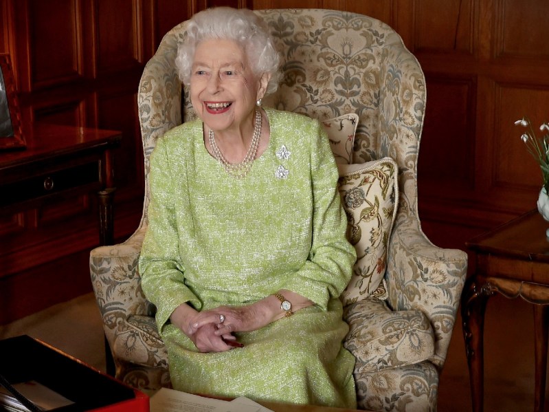 Queen Elizabeth wears a green gown as she sits in a living chair