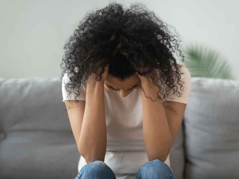 Stressed miserable black woman hold head in hands suffer from grief problem, depressed lonely upset african girl crying alone on sofa at home troubled with pregnancy regret mistake abortion concept