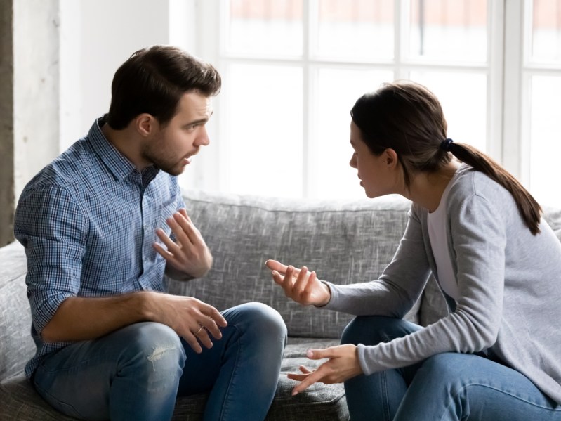 Stressed young married family couple arguing emotionally, blaming lecturing each other, sitting on couch