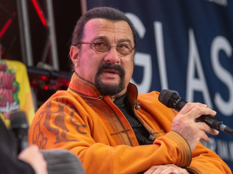 Steven Seagal wearing yellow jacket speaking into microphone