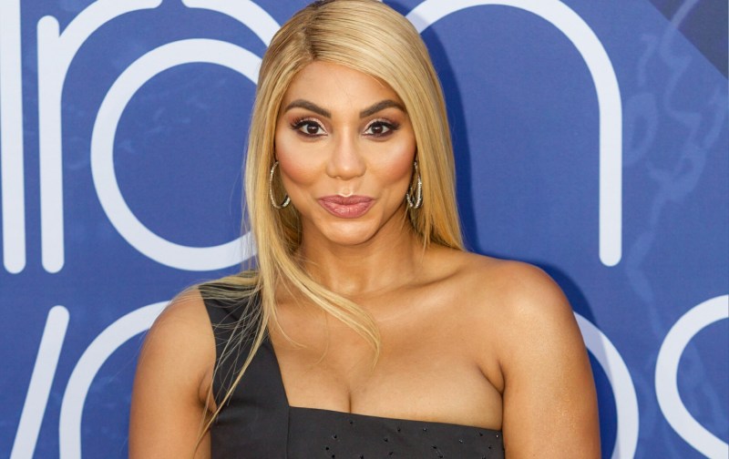 Tamar Braxton wears a one strap black dress against a blue background on the red carpet