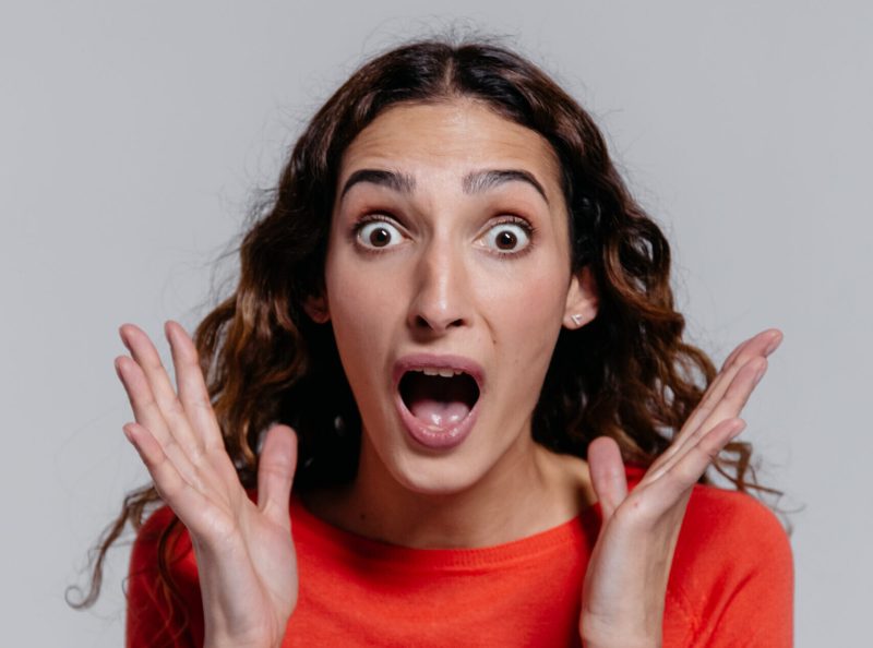 Woman in orange crew neck long sleeve shirt feeling surprised