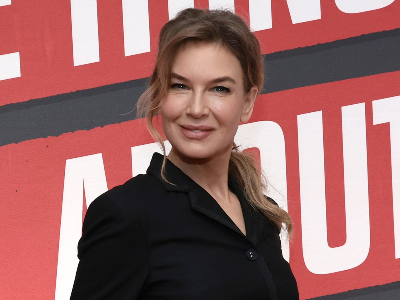 Renee Zellweger wearing black blazer smiling with ponytail