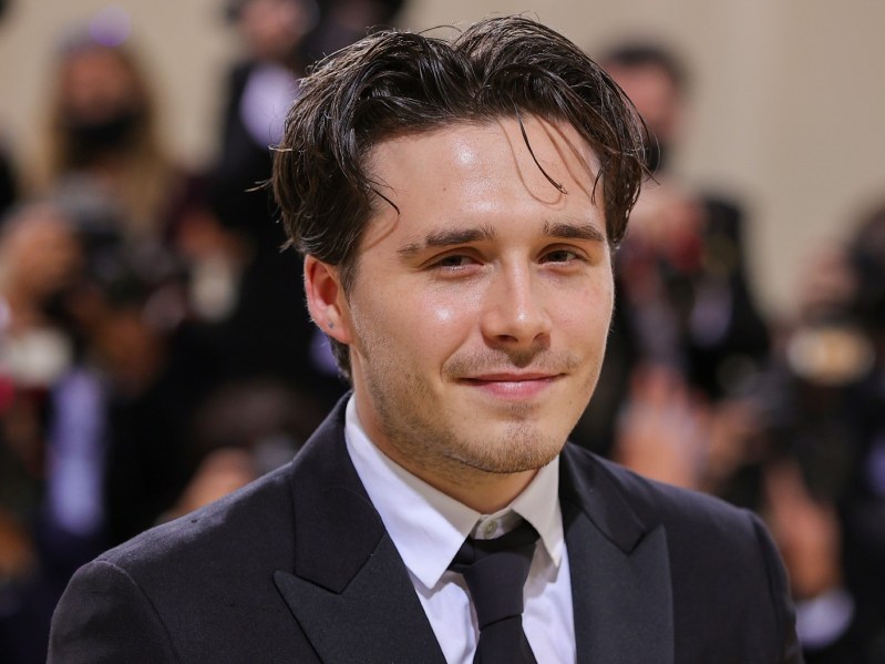 Closeup of Brooklyn Beckham smiling wearing black suit and tie