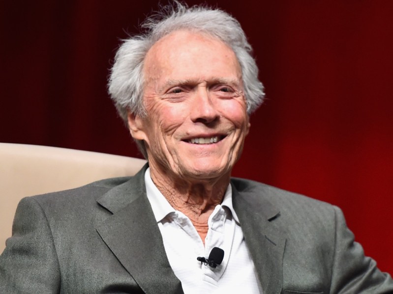 Clint Eastwood wears a gray suit jacket as he sits onstage