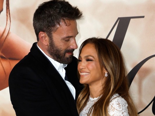 Ben Affleck, in a black suit, cozies up with Jennifer Lopez, in a white dress, on the red carpet