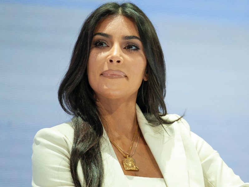 Kim Kardashian wears a white blazer over a white top while listening on stage
