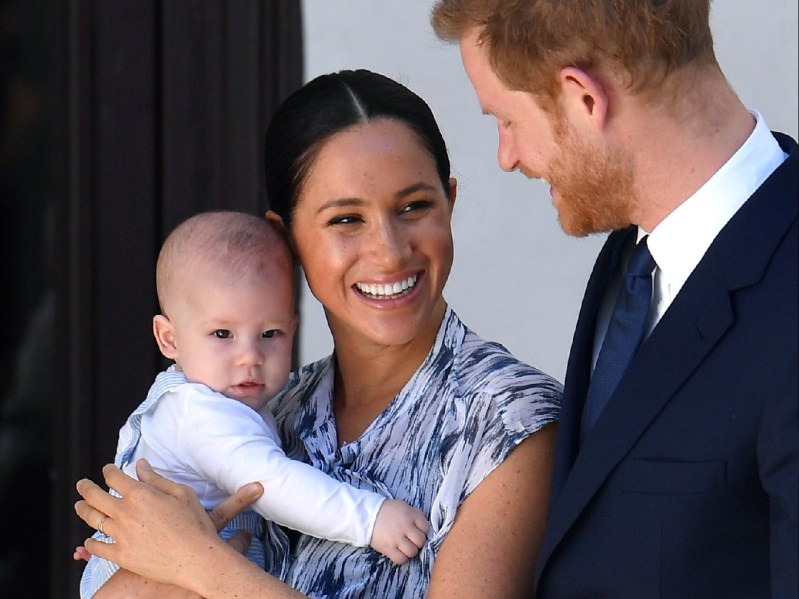Meghan Markle holds son Archie as Prince Harry, in a dark suit, looks on with a smile