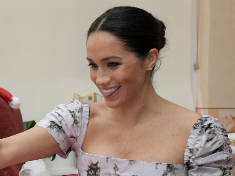 Meghan Markle playfully bites her tongue while wearing a flowery dress at a charity visit
