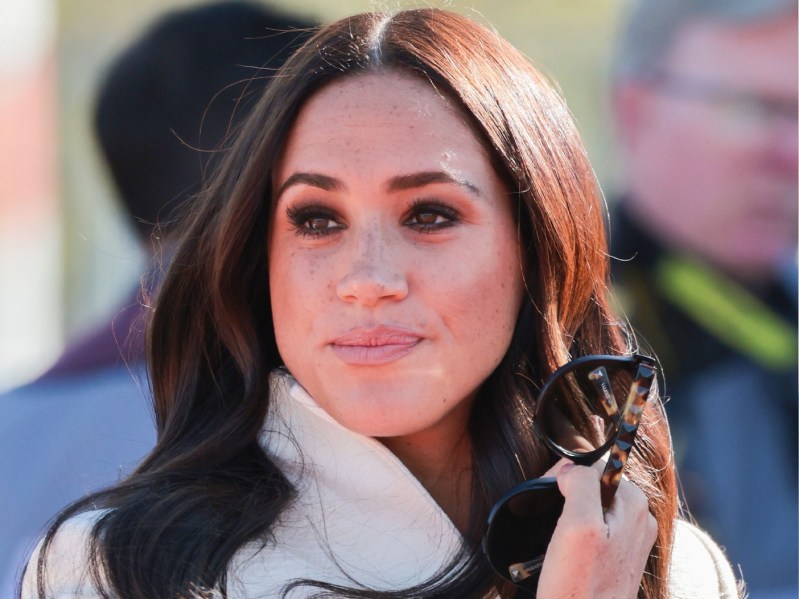 Meghan Markle holds a pair of sunglasses while wearing a white coat at the Invictus Games