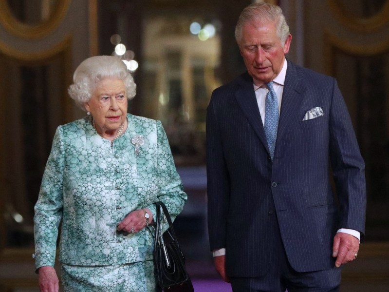 Queen Elizabeth, in a green and white dress suit, walks with son and heir Prince Charles, in a dark suit