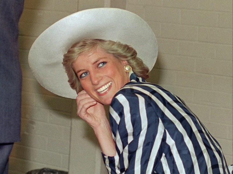 Princess Diana wears a white hat and a blue and white stripped dress against a beige background