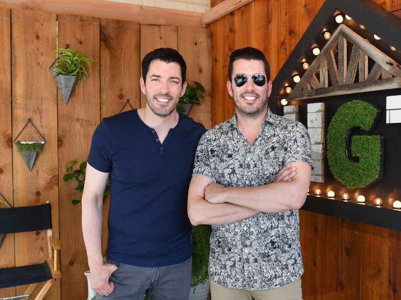The Property Brothers standing side-by-side in front of wood panelling