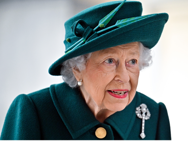 Close up of Queen Elizabeth wearing deep teal suit and hat and looking off-camera to the right
