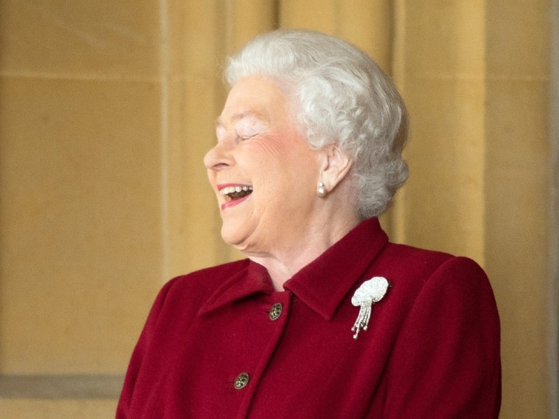 Queen Elizabeth wearing burgundy suit jacket and laughing