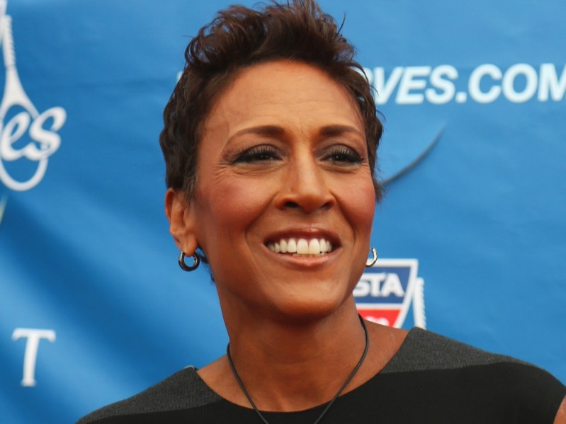 Closeup of Robin Roberts wearing black top with pixie cut in front of blue background