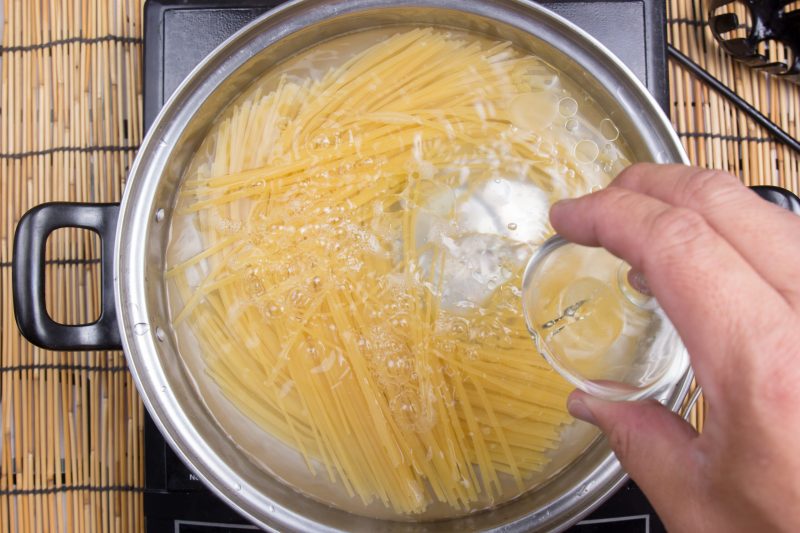 Olive oil being poured into a pot with pasta.