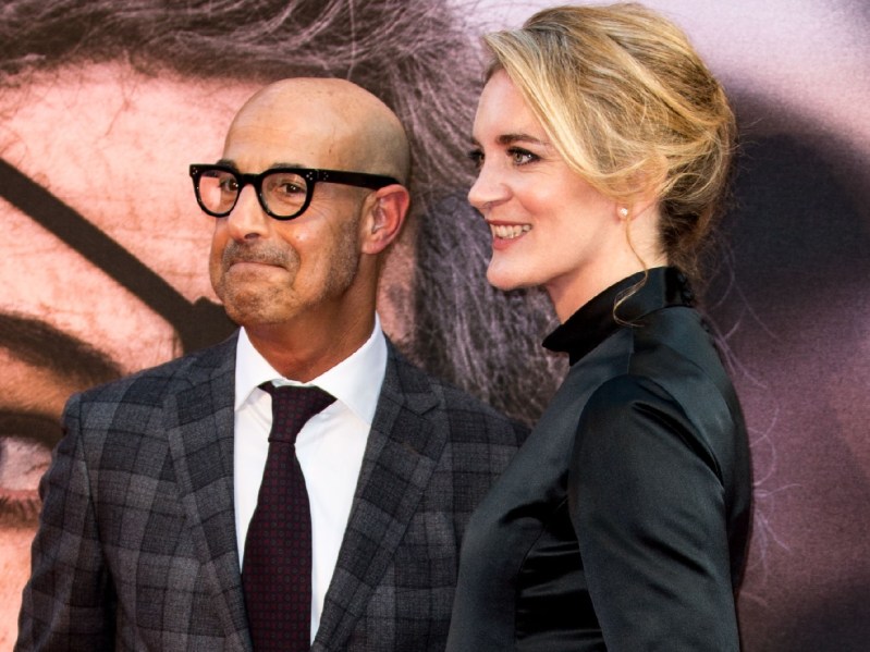 Stanley Tucci wears a plaid suit and stands with wife Felicity Blunt, in a black dress, on the red carpet