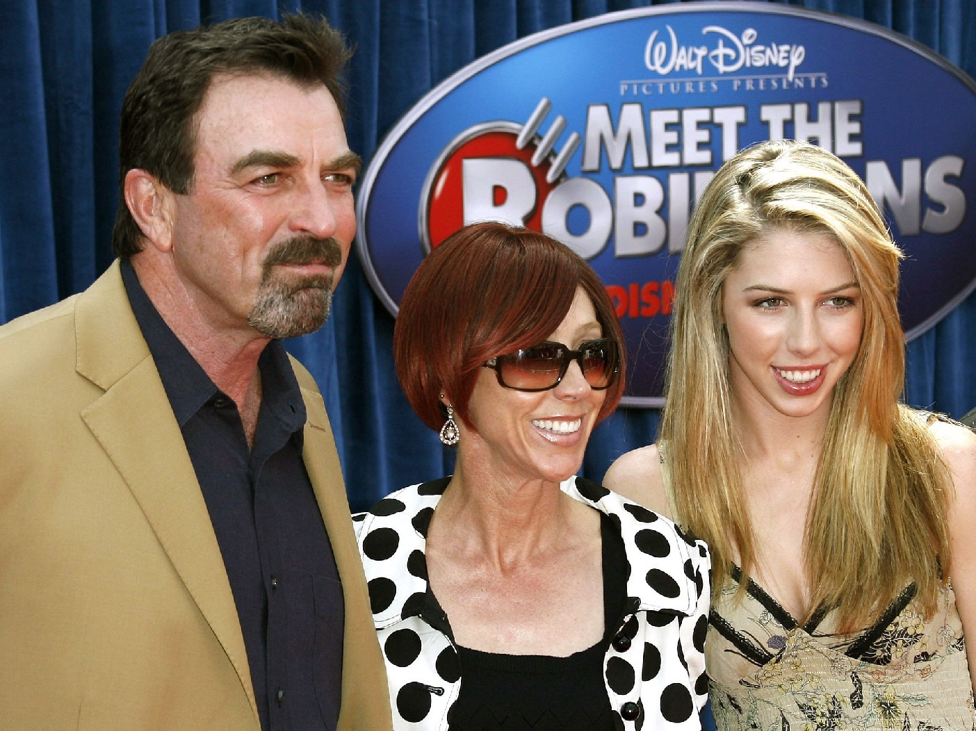 Tom Selleck, in a beige jacket, stands with wife Jillie Mack, in black and white polka dots, and daughter Hannah on the red carpet