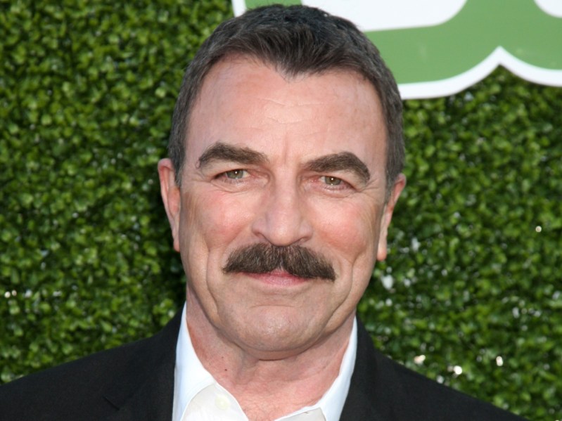 Closeup of Tom Selleck smiling wearing white collared shirt and black blazer