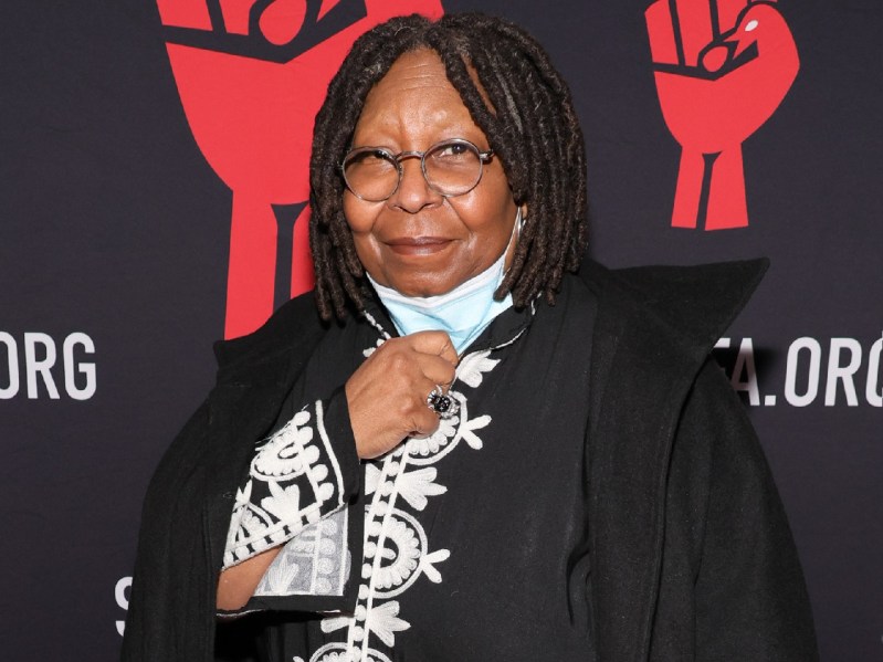Whoopi Goldberg pulls down her face mask as she walks the red carpet wearing a black and white tunic
