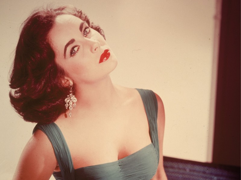 Modeling photo of Elizabeth Taylor circa 1950s with shoulder length hair and bright red lipstick.