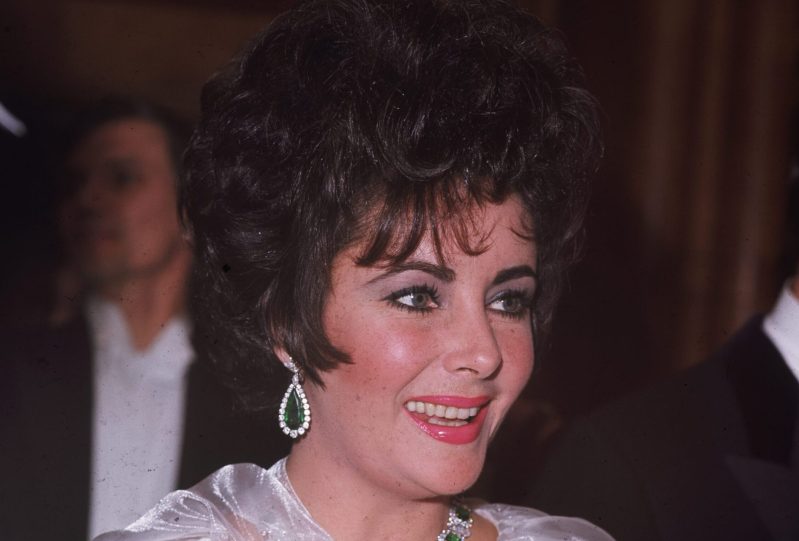 Close up of Elizabeth Taylor sporting emerald and diamond jewels at an event in 1967.