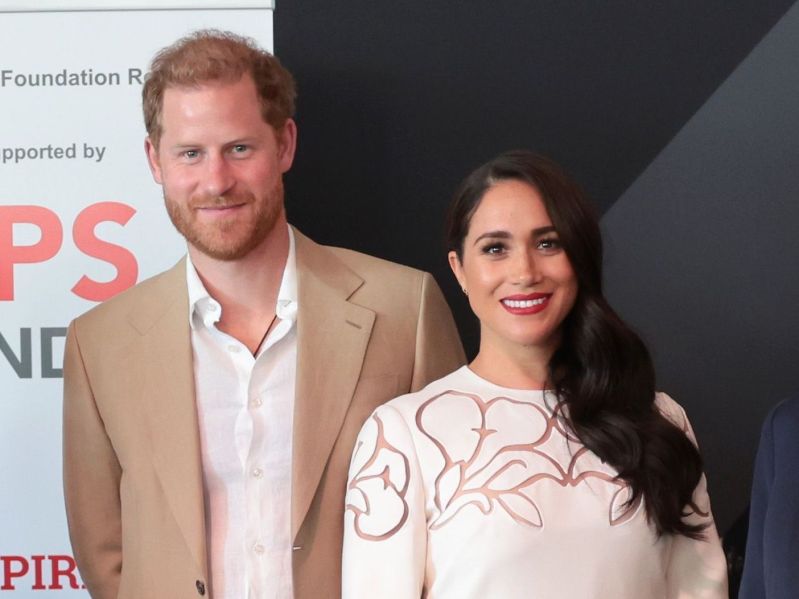 Prince Harry in a tan suit with Meghan Markle in a white dress